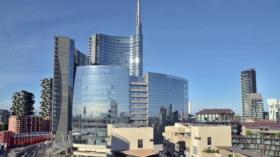 A modern cityscape with a prominent curved skyscraper, a tall tower, and surrounding residential buildings.