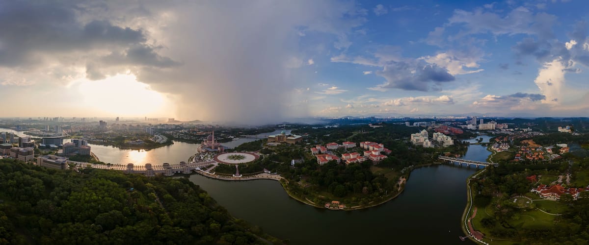 A panoramic view of a city with a river, bridges, and a park with red-roofed buildings.