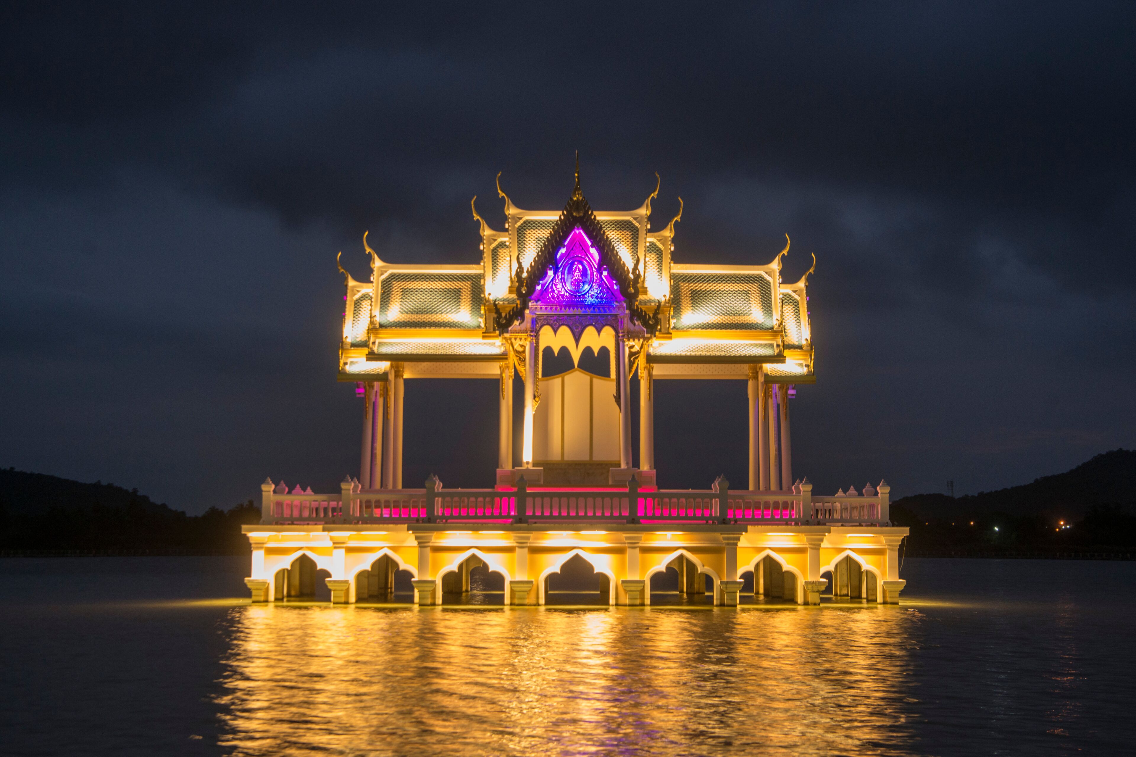 A brightly lit temple with a central spire and ornate architecture, situated on a waterfront.