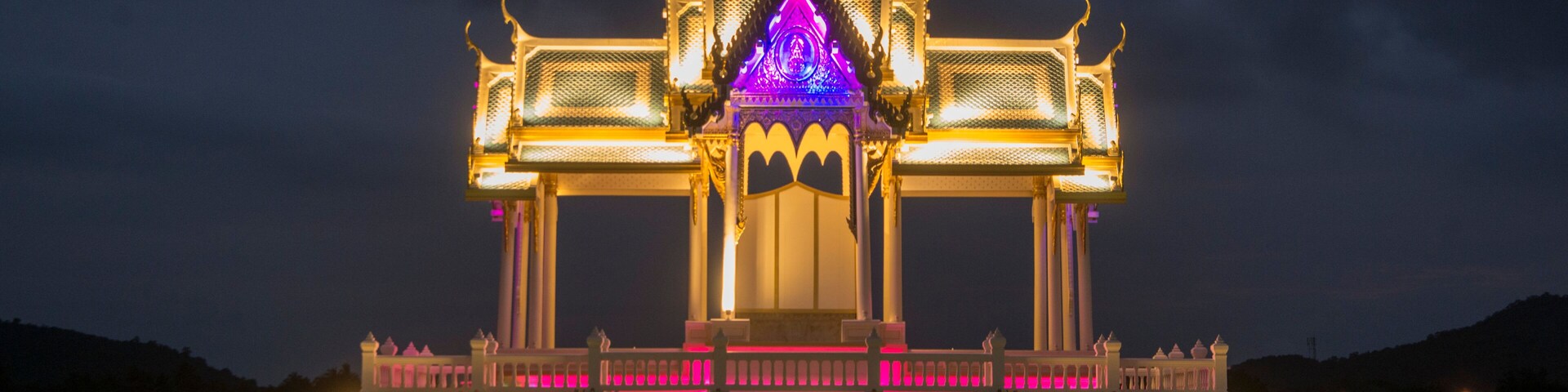 A brightly lit temple with a central spire and ornate architecture, situated on a waterfront.