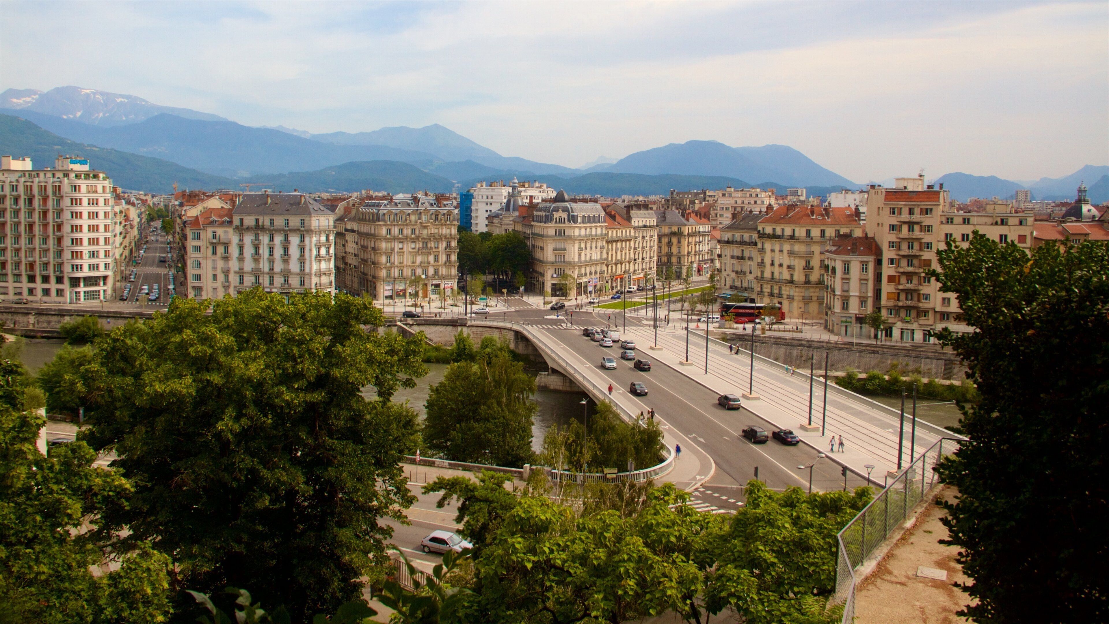 A cityscape with a river, a bridge, and mountains in the background.