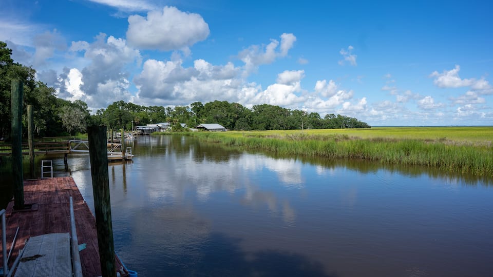 A calm river with a dock, surrounded by lush greenery and a clear blue sky.