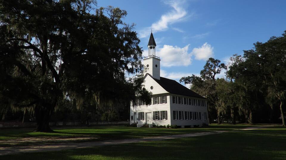 A white church with a steeple, surrounded by trees and a clear blue sky.