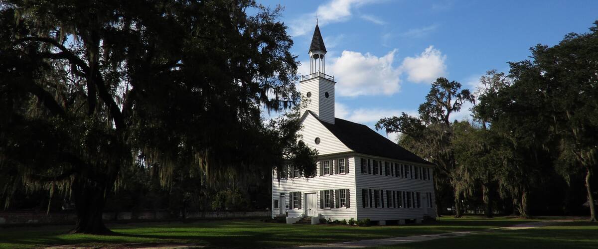 A white church with a steeple, surrounded by trees and a clear blue sky.