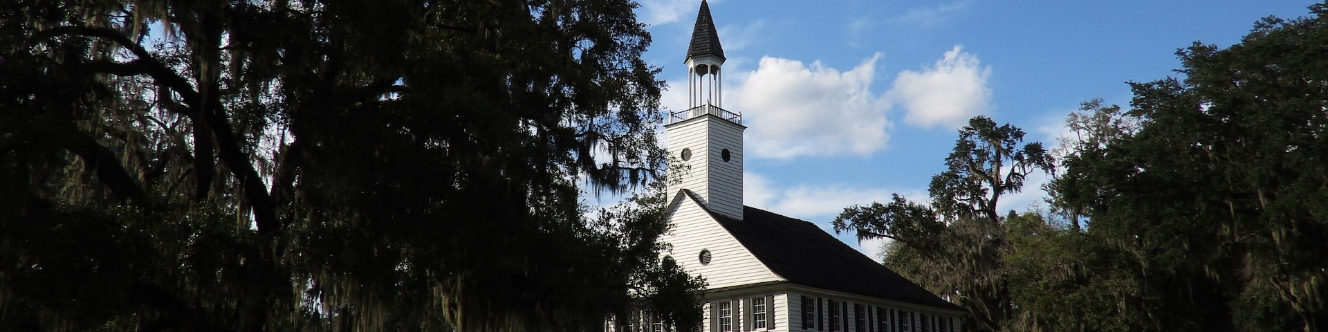 A white church with a steeple, surrounded by trees and a clear blue sky.