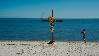 Boy with football beside Cross on the sandy beach with a boat in background in Cedar Key , Florida and boy on right side. Sunny Day with blue sky and calm waters.