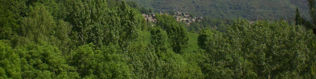 Une vallée abritant un petit village, entourée de collines verdoyantes et bordée, au loin, de montagnes aux sommets enneigés, le tout sous un ciel bleu et dégagé.