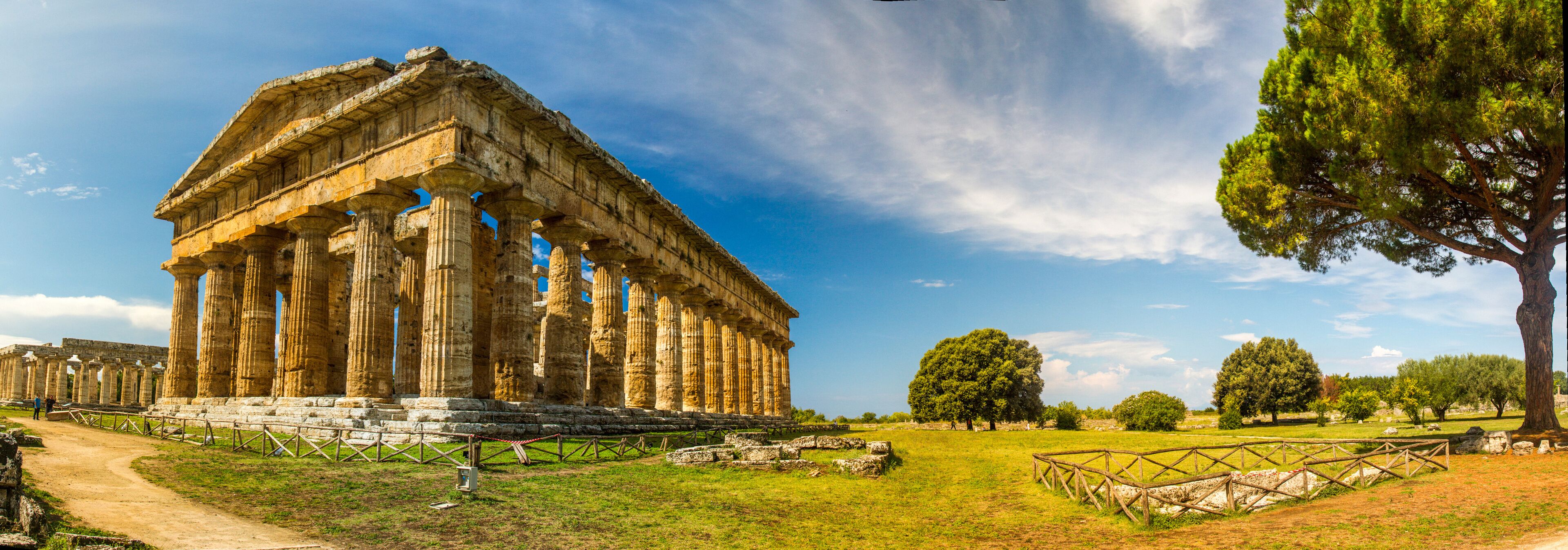 An ancient Greek temple with columns, surrounded by a grassy field and trees.