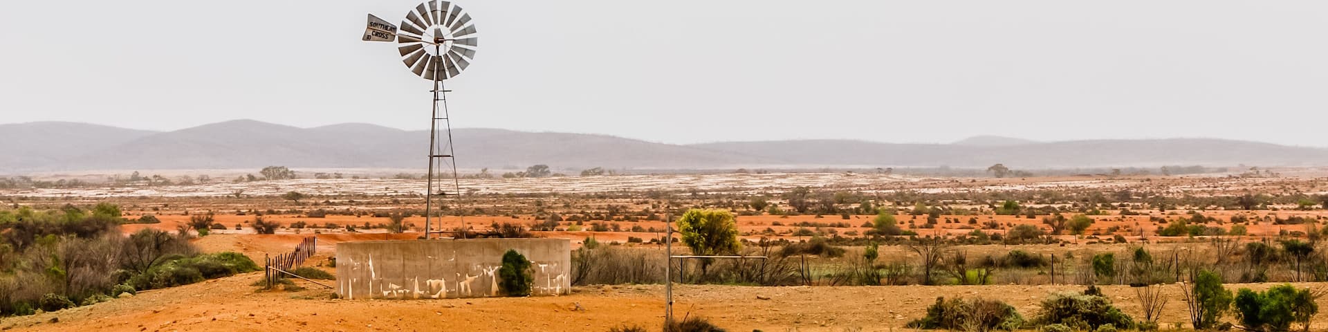 A windmill in a desert landscape with distant mountains.