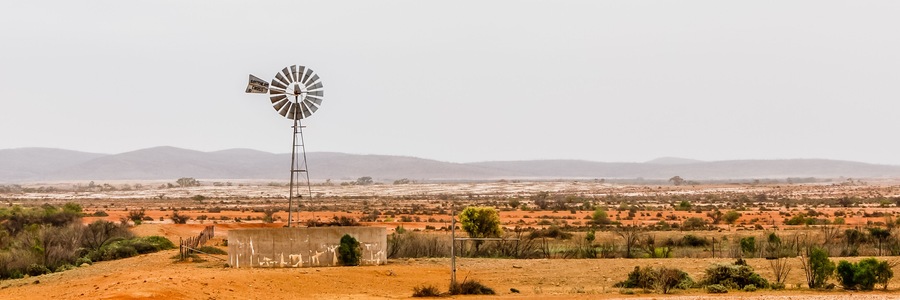 A windmill in a desert landscape with distant mountains.