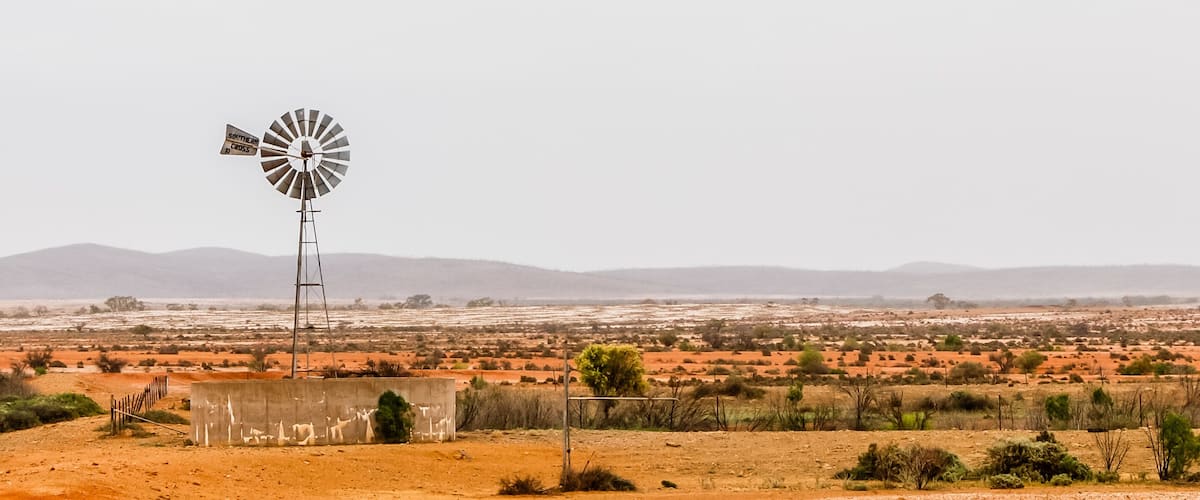 A windmill in a desert landscape with distant mountains.