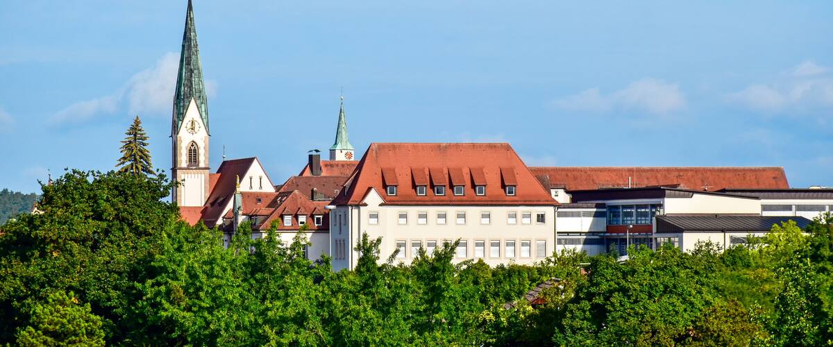 A church with a tall steeple and a clock tower, surrounded by buildings and trees.