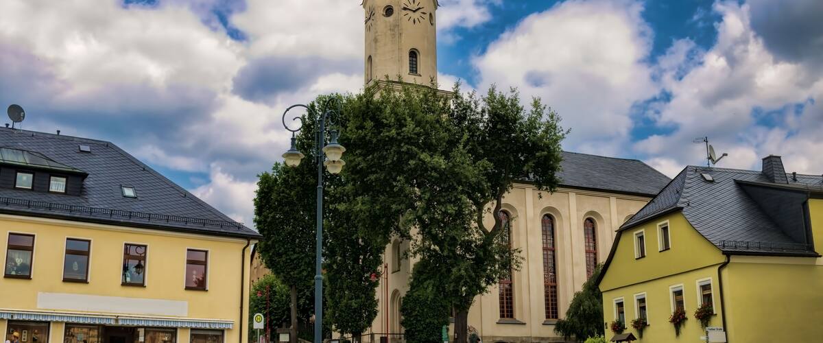 A church with a clock tower, surrounded by buildings and trees.