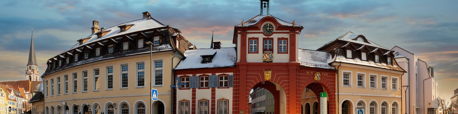 Um edifício histórico com uma torre de relógio, entradas em arco e neve no telhado.
