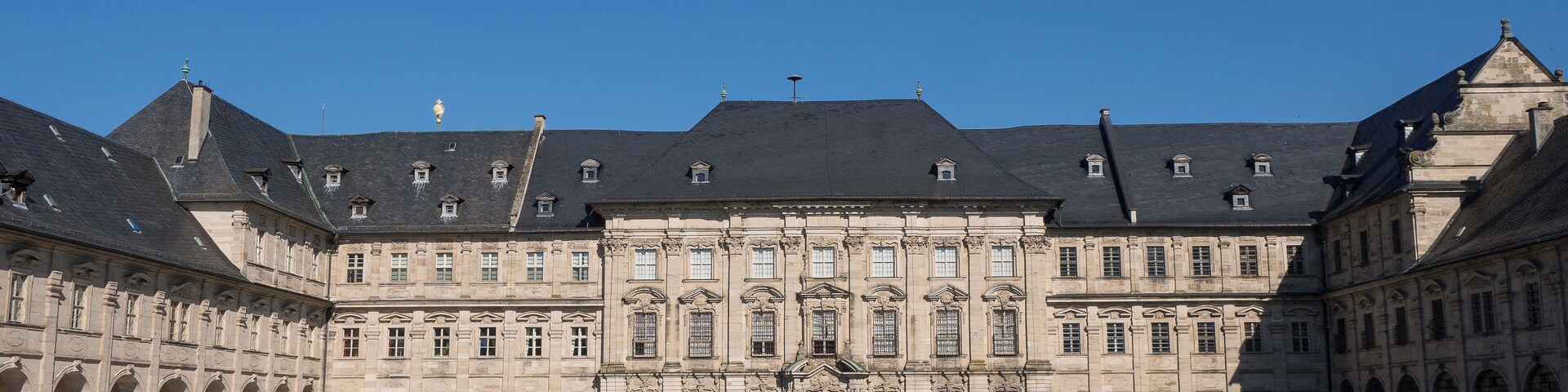 A historic building with a symmetrical facade, large windows, and a central courtyard with trimmed hedges.