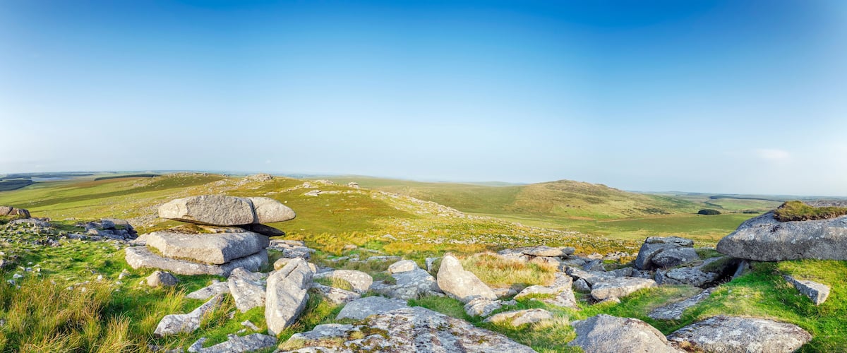 A mountainous landscape with large boulders and grassy fields under a clear sky.