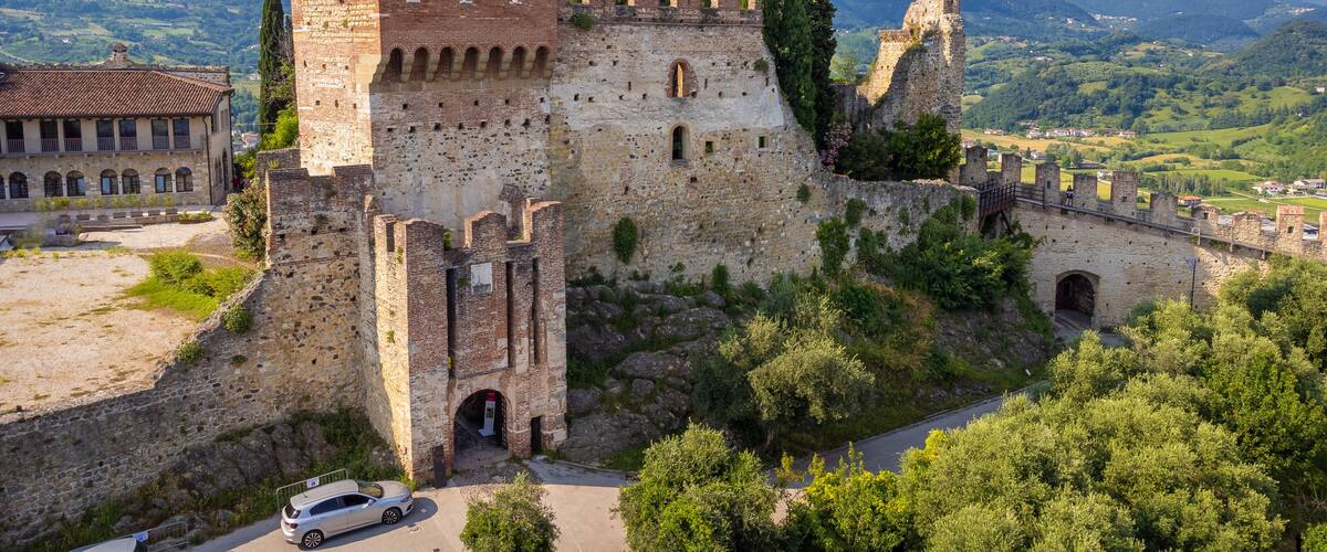 A historic castle with a prominent tower, surrounded by lush greenery and rolling hills in the background.