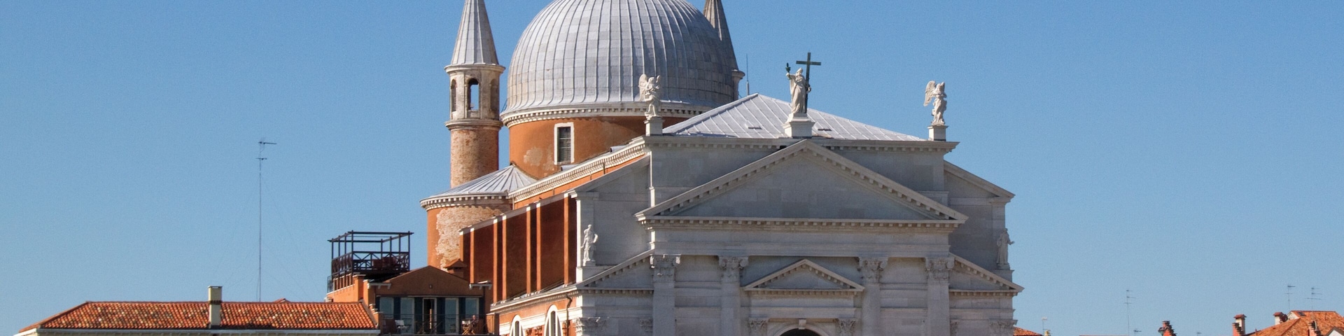 Una iglesia histórica con una cúpula grande y torres de campanas, rodeada de edificios venecianos tradicionales.