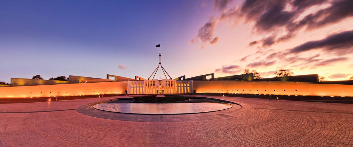 A modern architectural structure with a central building and a circular plaza, set against a sunset sky.