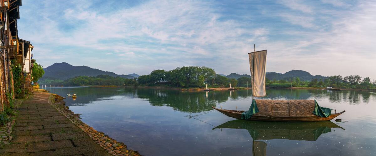 A calm river with a traditional boat, a stone pathway, and distant mountains.