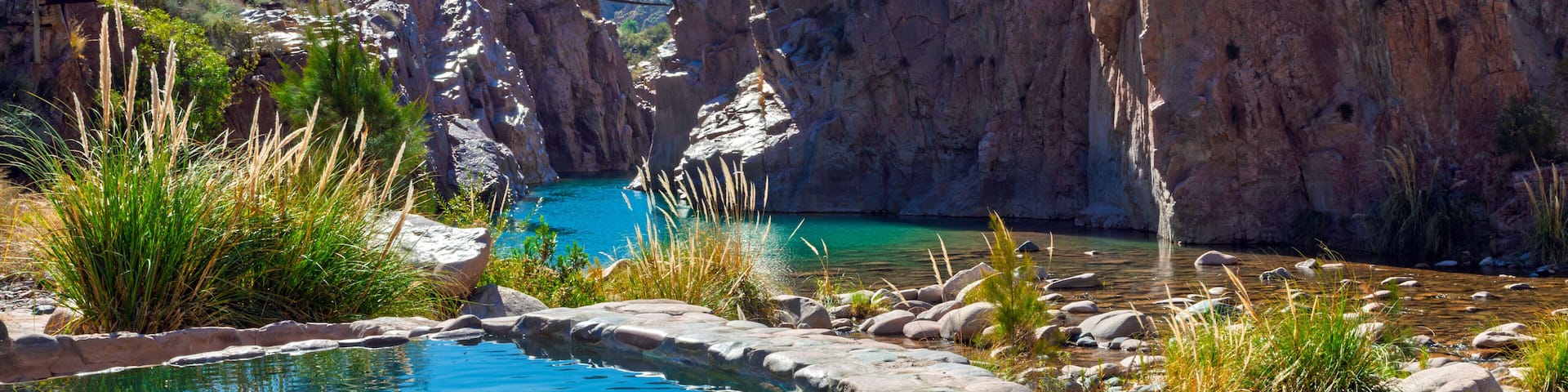 A clear blue pool surrounded by rocky terrain and sparse vegetation.