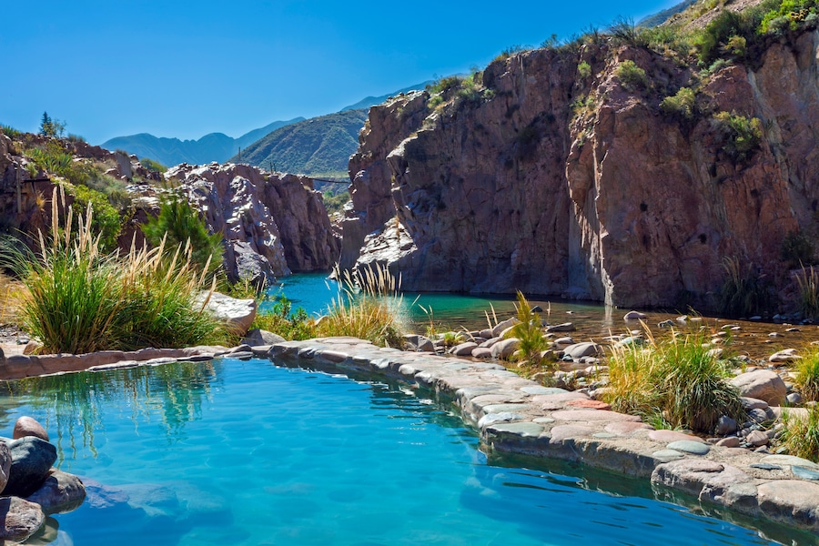 Une piscine d’eau cristalline, entourée d’un paysage rocheux et d’une végétation clairsemée.