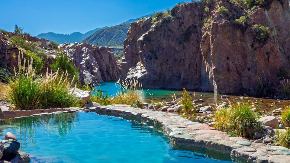 A clear blue pool surrounded by rocky terrain and sparse vegetation.