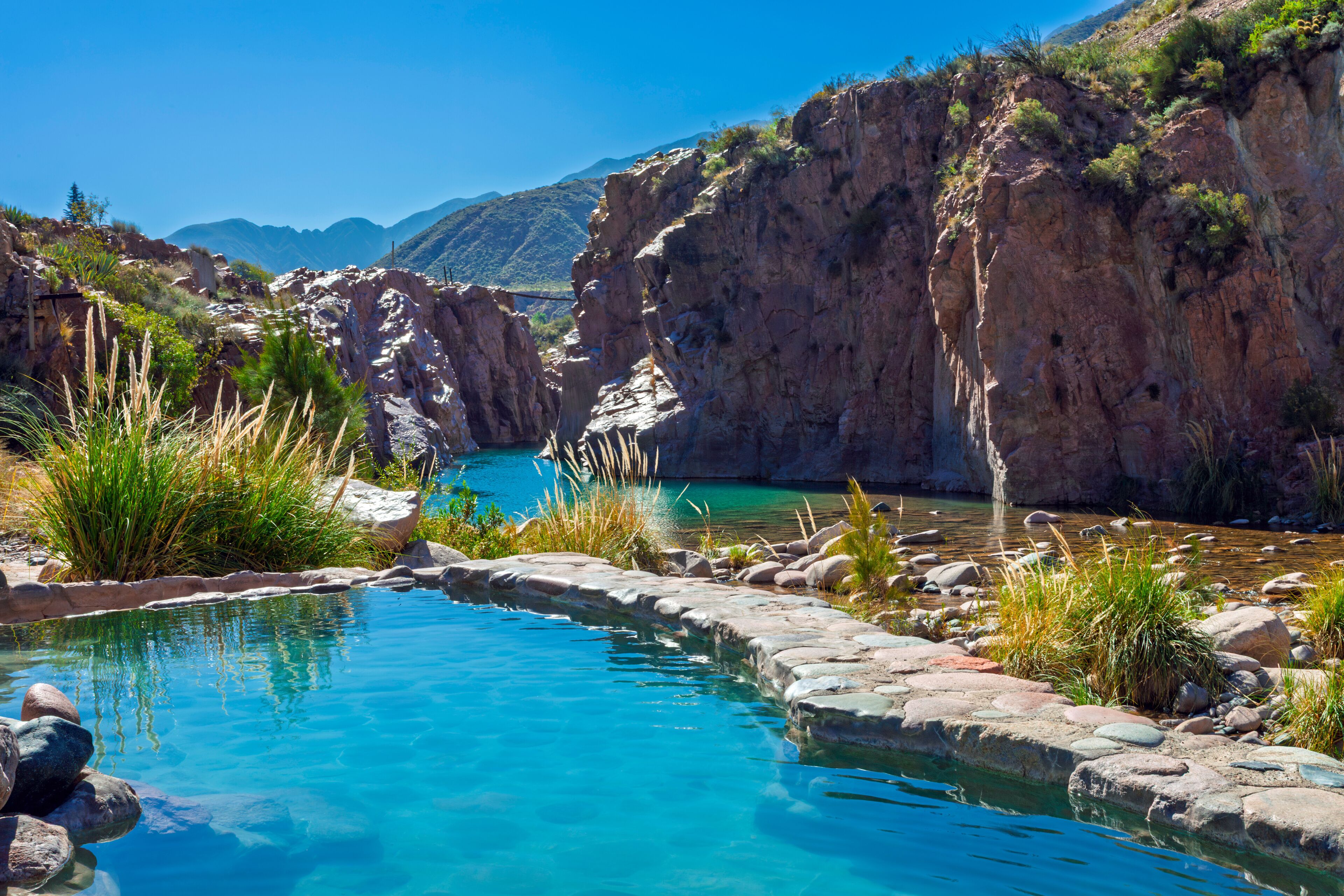 A clear blue pool surrounded by rocky terrain and sparse vegetation.