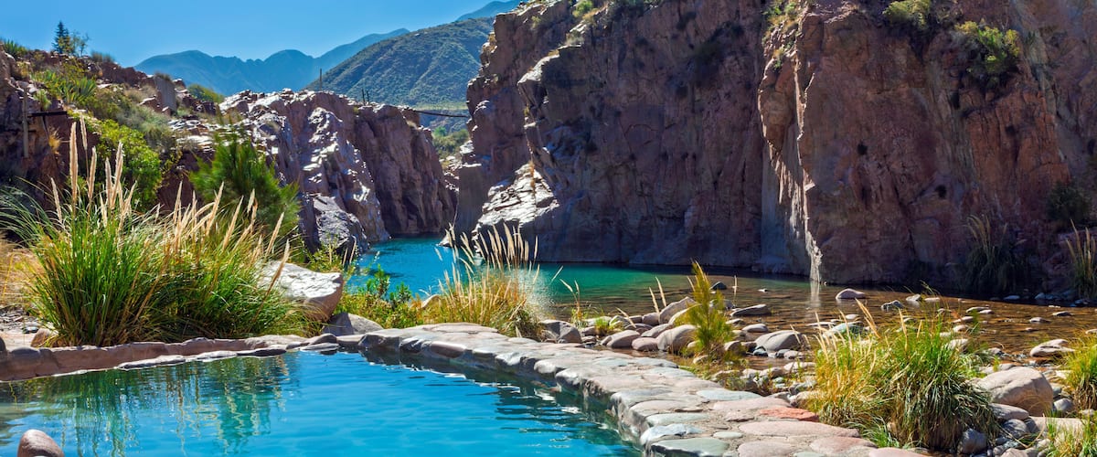 A clear blue pool surrounded by rocky terrain and sparse vegetation.