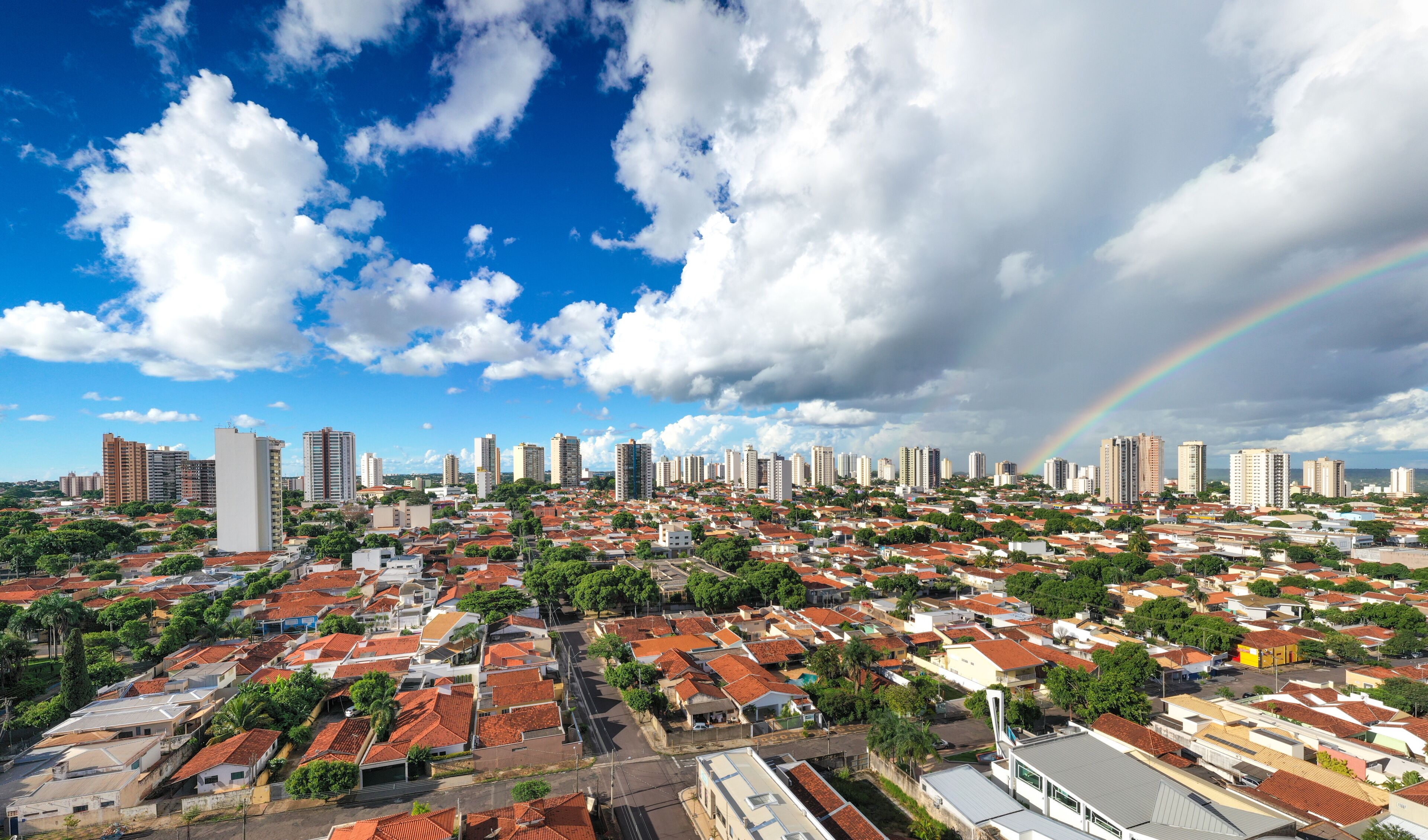 A cityscape with a rainbow, red-roofed houses, and tall buildings.