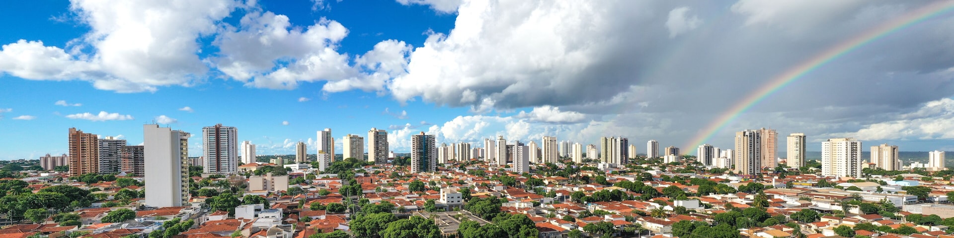 Paisagem urbana com arco-íris, casas de telhado vermelho e edifícios altos.