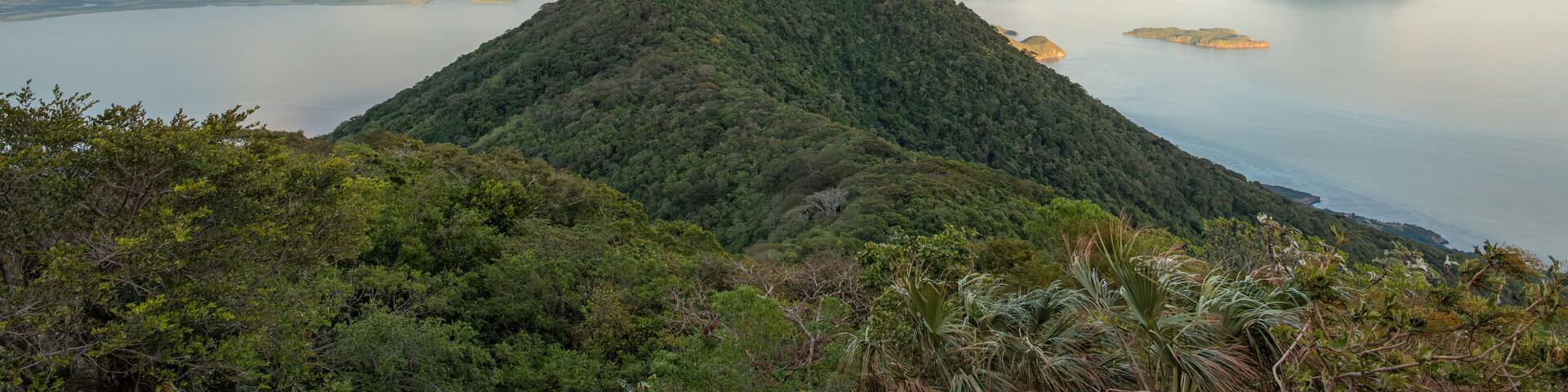 A mountain with lush greenery, a body of water, and distant islands.