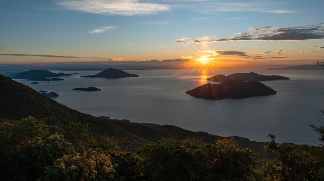 A sunset over a calm sea with several islands, surrounded by hills.