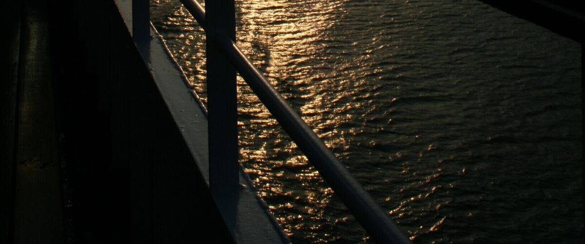 A boat on a river with mountains on both sides and the sun setting in the background.