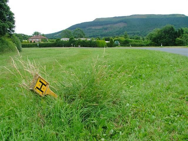 A grassy field with a yellow sign in the foreground and a road in the background.