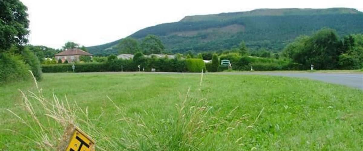 A grassy field with a yellow sign in the foreground and a road in the background.