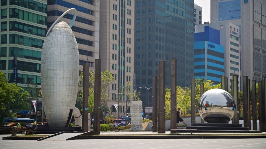 A modern urban plaza with a large, curved sculpture, tall buildings, and a reflective sphere.