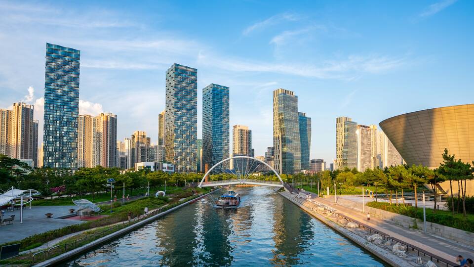 A river with a bridge, surrounded by modern skyscrapers and greenery.