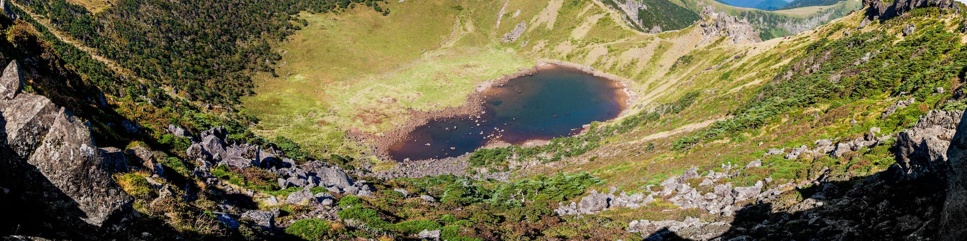 A crater lake surrounded by rugged mountains and lush greenery.
