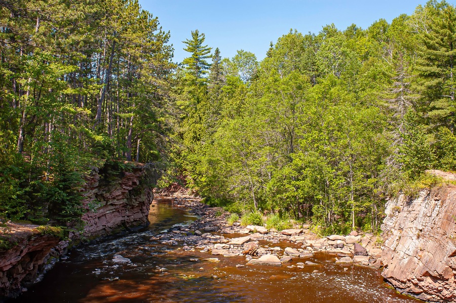 Ein Fluss fließt durch einen Wald mit steilen, felsigen Klippen und dichtem Grün.
