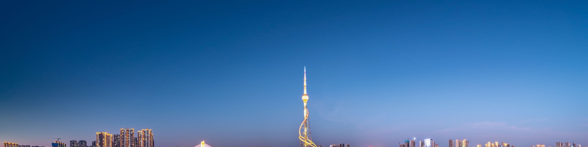 A city skyline with a prominent tower and a bridge reflecting on the water.