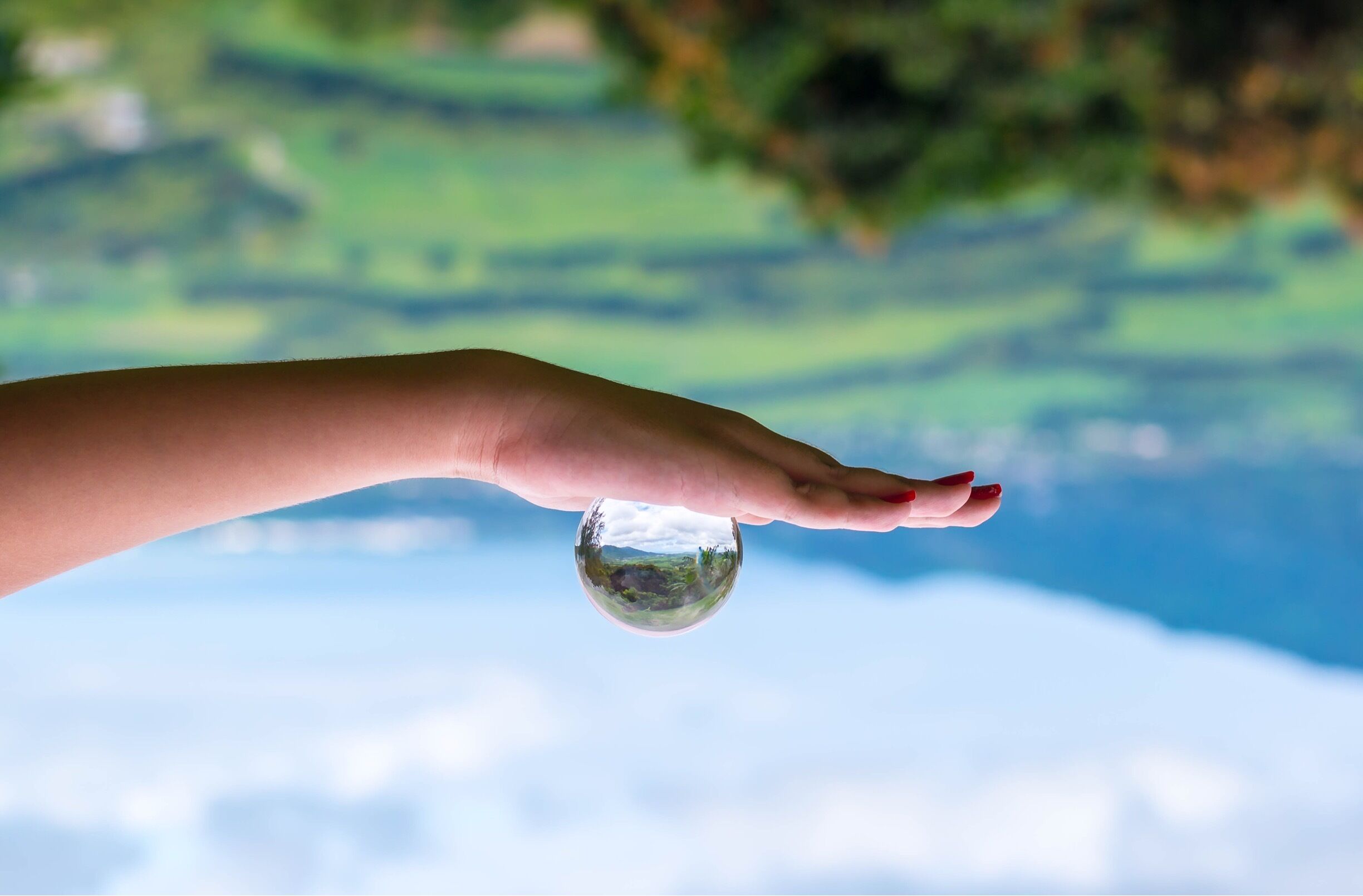 A hand holding a clear glass sphere with a landscape reflection.