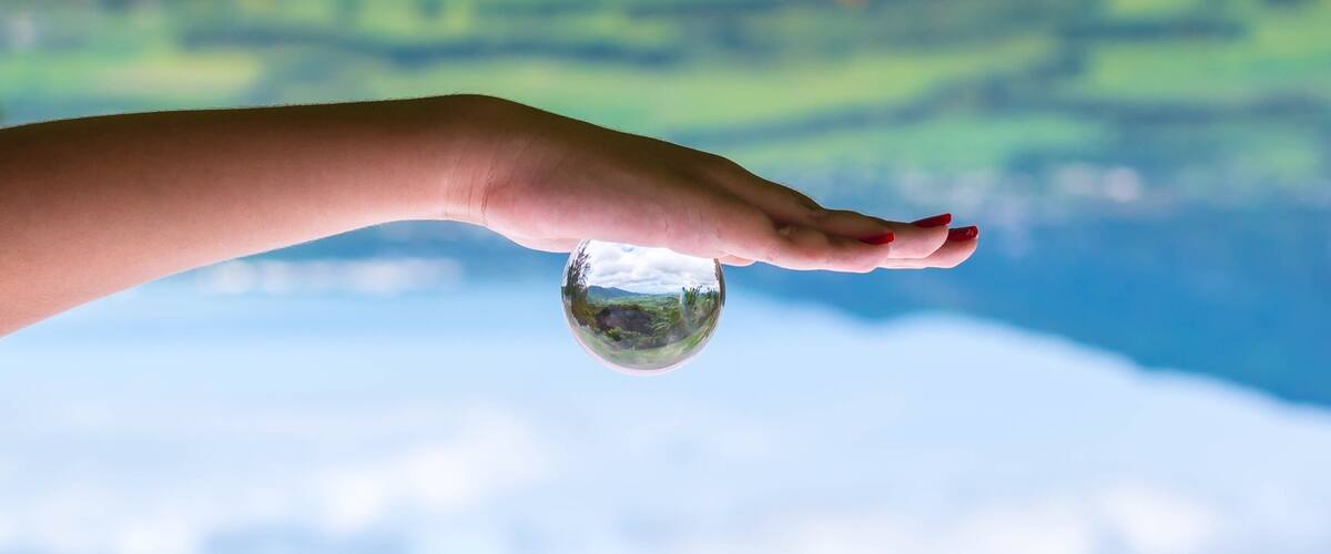 A hand holding a clear glass sphere with a landscape reflection.