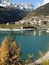 A mountain town by a lake with autumn foliage and snow-capped peaks.