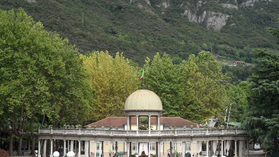 A historical building with a dome, surrounded by lush greenery and a mountainous backdrop.
