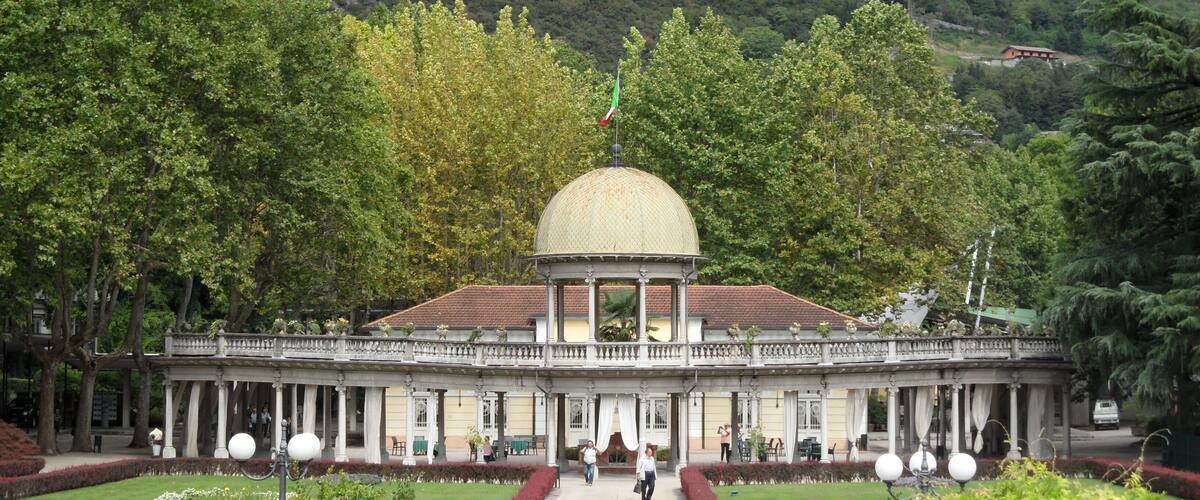 A historical building with a dome, surrounded by lush greenery and a mountainous backdrop.