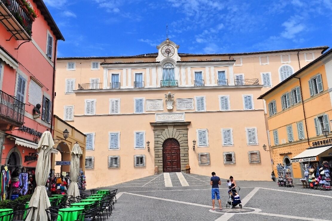 A historic building with a clock tower, a central entrance, and surrounding shops.