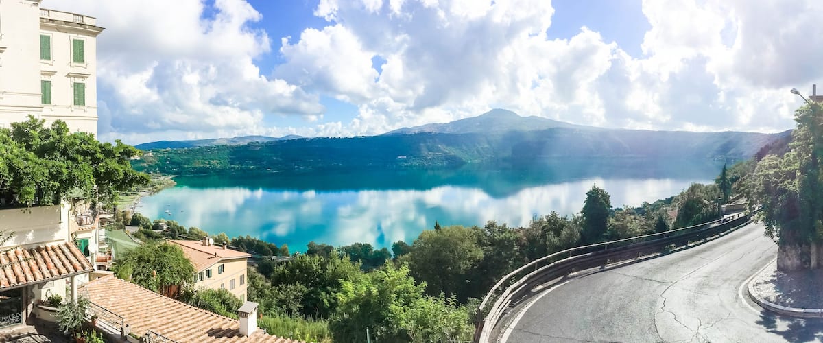 A lake surrounded by mountains, a winding road, and buildings with green shutters.