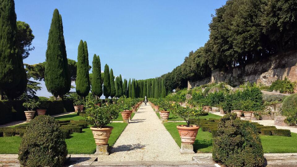 A formal garden with a gravel pathway flanked by tall cypress trees and terracotta planters.