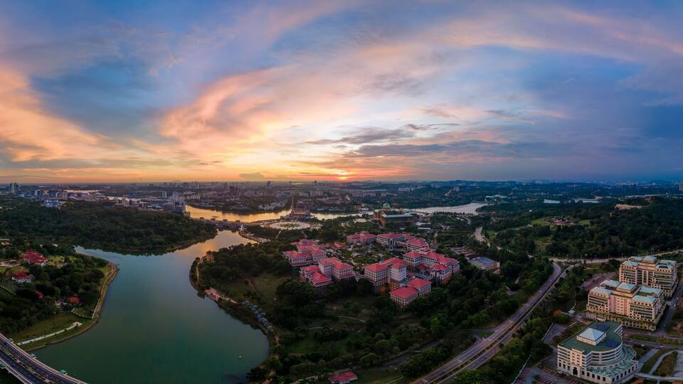 A panoramic view of a city with a river, green areas, and modern buildings.
